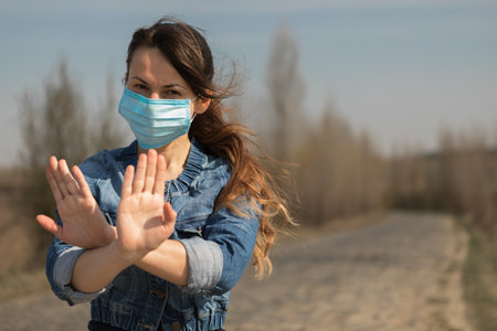 Woman in protective sterile medical mask on her face looking at camera outdoors. Hand stop Sign . Pandemic coronavirus concept.の写真素材