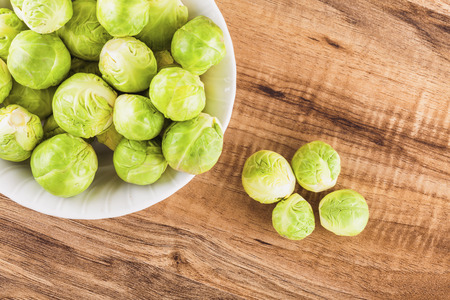 Overhead shot of brussels sprouts in a ceramic bowl and on a wooden table.の写真素材