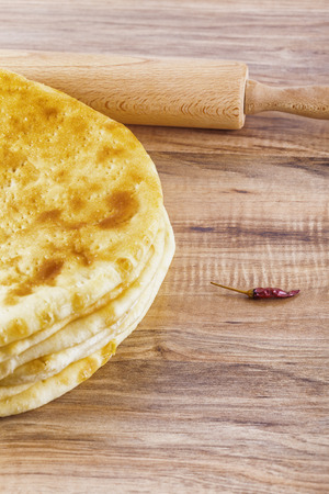 Hogh angle shot of a baked pastry dish, hot pepper and a rolling pin placed on a wooden talbeの写真素材