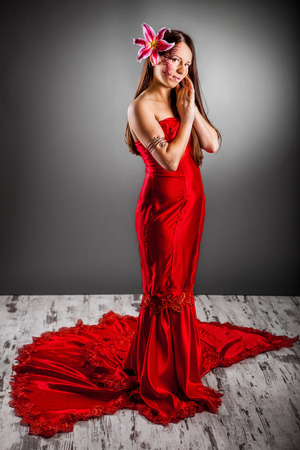Photo of a beautiful girl in a red dress posing with open arms on a red and gray backgroundの写真素材