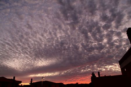 Dramatic sky at sunset with strong color and soft clouds above the urban roofsの写真素材