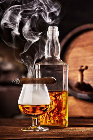 Glass of cognac or brandy with smoking cigar on wooden table.Glass ful of smokeの写真素材