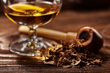 tobacco and drefocused glass of cognac and pipe on wooden tableの写真素材