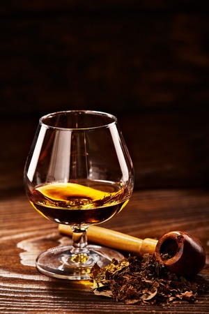 Glass of cognac and pipe with tobacco on wooden tableの写真素材