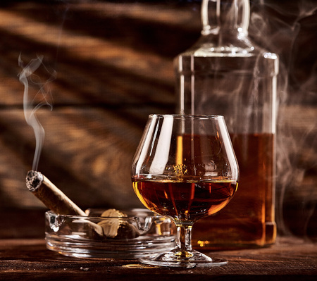 Glass of cognac or brandy with smoking cigar on wooden tableの写真素材