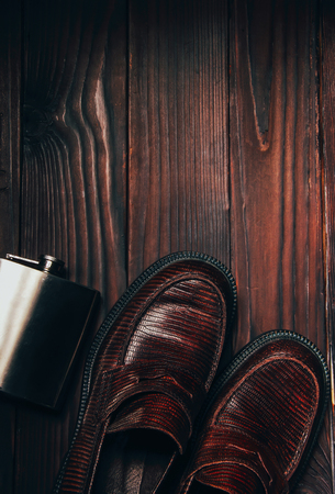 Mocasine shoes of snake skin and stainless flask on the woden floor with free space. Flat layの写真素材