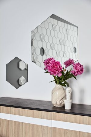 Vase with beautiful blooming peonies on wooden commode against white wall with hexagonal mirror .Background.の写真素材