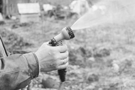 black and whiteMan turns on the hose for watering plants with a sprayer. include a spray bottle for...