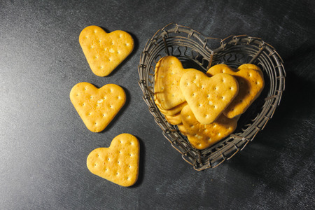 A heart cookie, in a vase in the shape of a heart on a dark background. A metal vase with cookies....