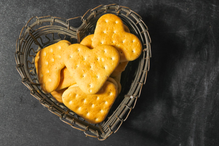 A heart cookie, in a vase in the shape of a heart on a dark background. A metal vase with cookies....
