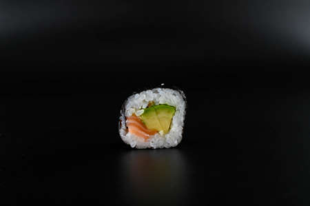Close-up of a piece of sushi with salmon and avocado on an isolated black background.の写真素材