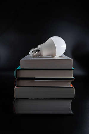 White led light bulb on a pile of books on an isolated black background.の写真素材