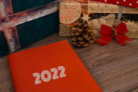 Book with 2022 on the cover on a wooden table with Christmas presents in background.