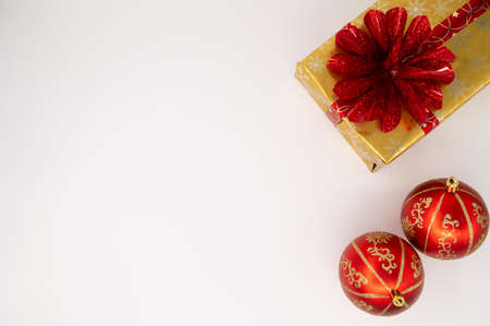 Close up of a gold Christmas gift box with red bouquet, wrapping tape and red Christmas bulbs on an...