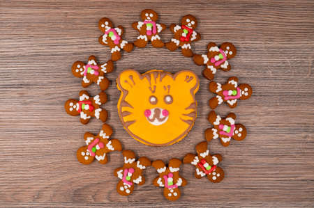 Gingerbread men with glaze put around the tiger-shaped orange gingerbread cookie on a wooden table. New year 2022 concept.の写真素材