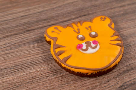 Close-up of a tiger-shaped gingerbread cookie with orange glaze on a wooden table.の写真素材