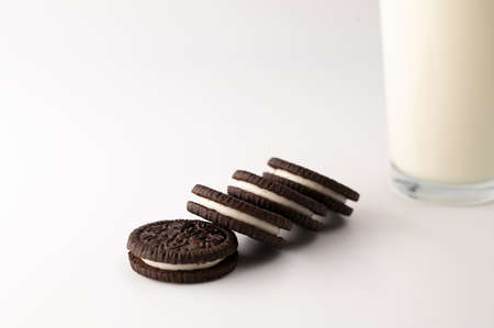 Close-up of a row of chocolate cream cookies next to glass full of milk on an isolated white background.の写真素材