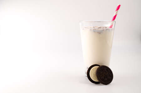 Milk with cookies in a glass with a pink straw, next to which is chocolate cream cookie cut in half on an isolated white background.. Copy space.の写真素材