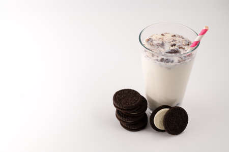Milk with cookies in a glass with a pink straw, next to which is a stack of chocolate cream cookies on an isolated white background. Top view. Copy space.の写真素材