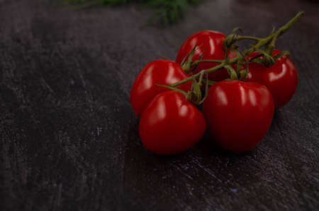 Close-up of a bunch of cherry tomatoes on a metallic dark background with herbs in the background.の写真素材