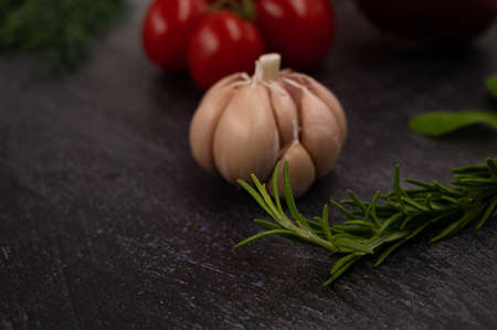 Close-up of a sprig of rosemary on a metallic dark background, with a head of garlic and other vegetables in the background.の写真素材