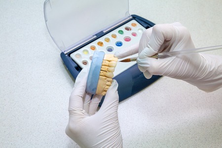 color matching on dentures. Paint brush with palette, gloved hands