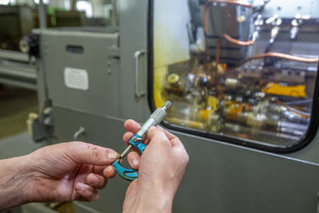 Hands of a man with a micrometer, measure the part against the background of the machine for the...