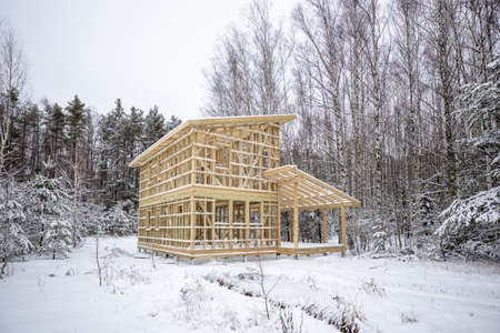 frame house construction in winter, under the snow, in the forest. Fresh wood, frame of a two-story...