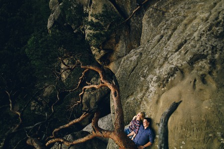 Young beautiful couple in jeans and shirts for a walk in the mountains. Woman and man lying in the sun on the rocksの写真素材