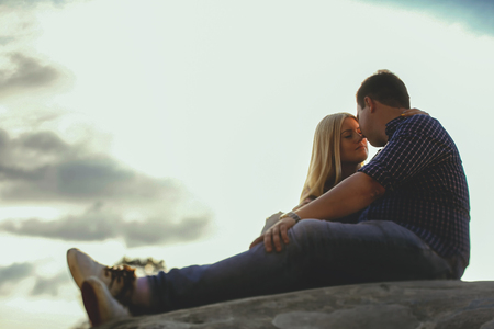 Young beautiful couple embracing in the mountains. Romantic kiss couple in love on the background of skyの写真素材