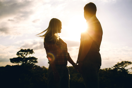Young beautiful couple in jeans and shirts for a walk in the mountains. The man and the woman against the backdrop of the setting sunの写真素材
