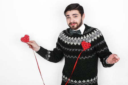 Young handsome bearded man in a knitted sweater with a decor in the form of hearts shows the situation alone on Valentine's Dayの写真素材