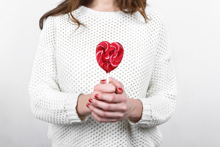 Girl in white sweater holding in hands sweet tasty lollipop in the shape of heart, St. Valentine's Dayの写真素材