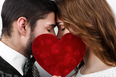 Stylish beautiful kissing young couple in love with red heart in hand, celebrating Valentine's Dayの写真素材