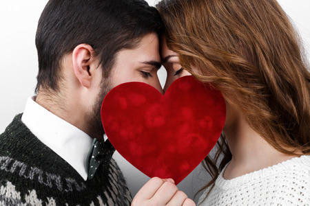 Stylish beautiful kissing young couple in love with red heart in hand, celebrating Valentine's Dayの写真素材
