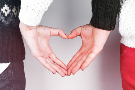 Stylish beautiful young couple in love with heart shaped hands, celebrating Valentine's Dayの写真素材