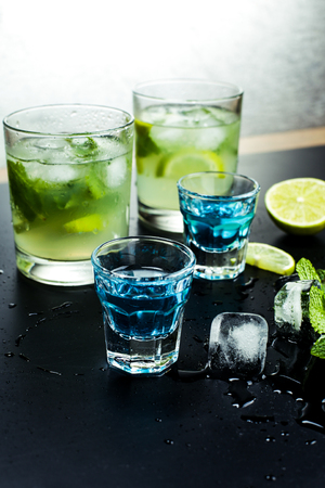 Tasty fragrant refreshing mojito with lime and mint on wet black table in bar or restaurant. Blue liqueur and cocktail mojito.の写真素材