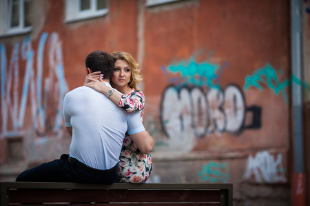 Happy, stylish newlywed couple posing on wooden bench in townの写真素材