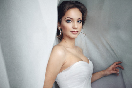 Beautiful sexy bride in white dress posing under curtainの写真素材