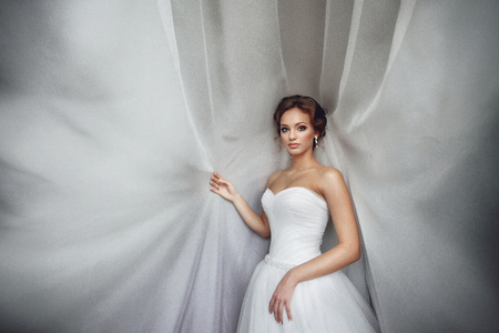 Beautiful sexy bride in white dress posing under curtainの写真素材