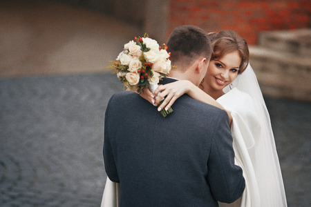 Happy newlywed couple with bouquet hugging outdoorsの写真素材