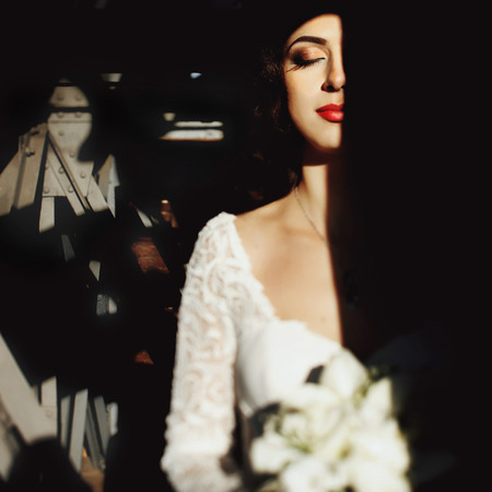 Bride with lily bouquet half in the shadow with industrial backgroundの写真素材