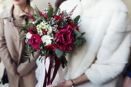 Bride in the fur coat holds red wedding bouquetの写真素材