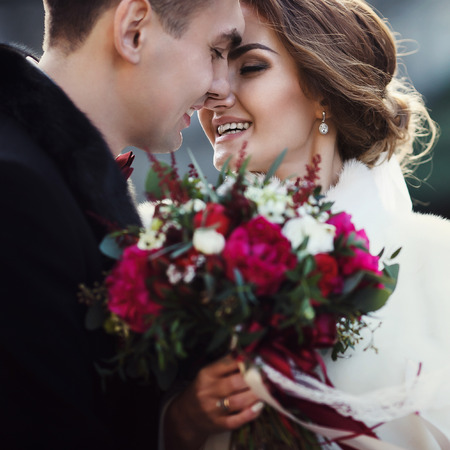 Newlyweds touch each other with noses, while bride holds a bouquetの写真素材