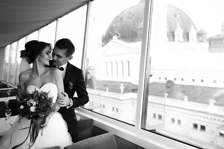 Bride and fiance in an empty restaurant hug before the windowsの写真素材