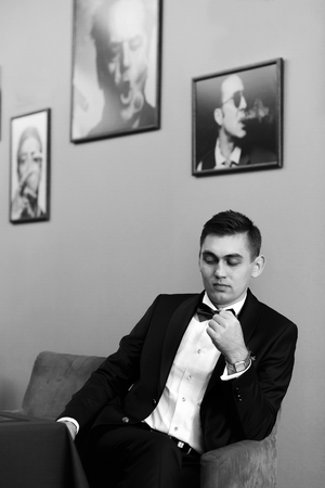 Bridegroom in tuxedo looks down while sitting in the chairの写真素材