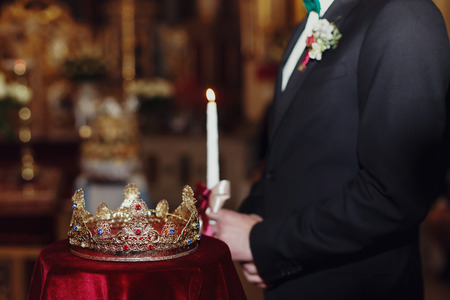 Crown lies on the red velvet while bridegroom stands on the background with candleの写真素材