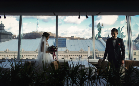Bride and fiance walk between empty tables in restaurant with great viewの写真素材
