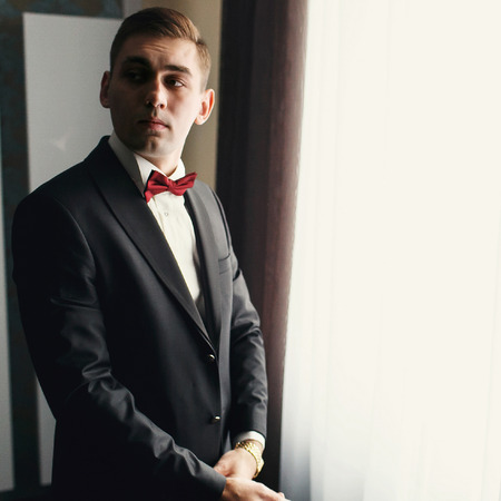 Young man in black suit and red bow tie looks over his shoulderの写真素材