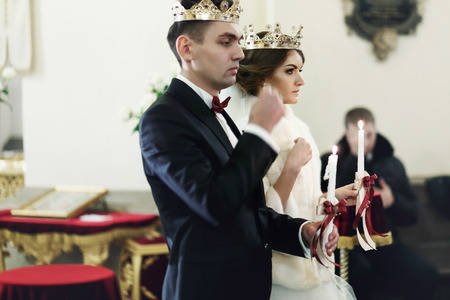 Bride and bridegroom standing in crowns during the ceremony in the churchの写真素材